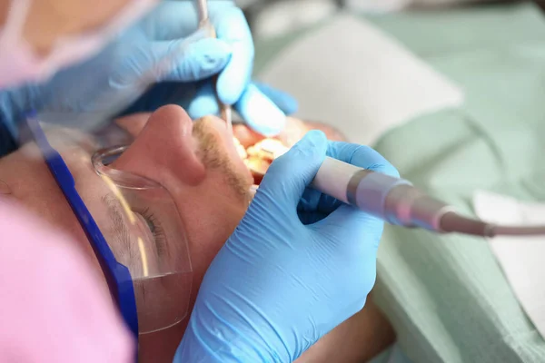 Врач-дантист лечит зубы молодого человека в клинике крупным планом — стоковое фото