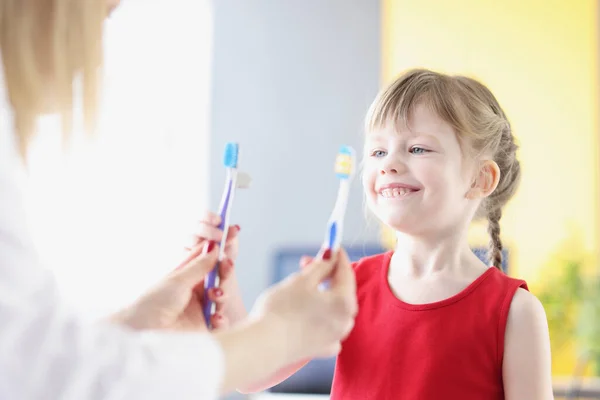 A kislány fogkefét választ a klinikán. — Stock Fotó