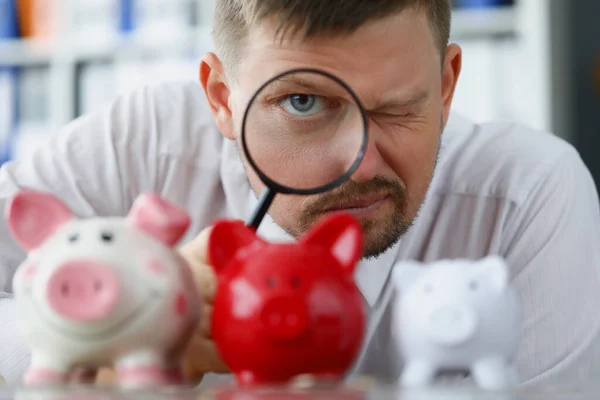 Mann blickt durch Lupe auf Sparschwein — Stockfoto