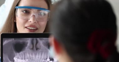 Dişçi doktor 4K filminin önündeki dijital tablette dişlerin panoramik resmine bakıyor.