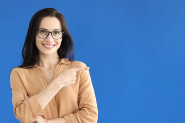 Gözlüklü kadın mavi arkaplandaki boşluğa parmağını gösteriyor