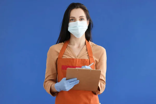 Mujer camarera en máscara protectora y guantes anotando orden sobre fondo azul — Foto de Stock