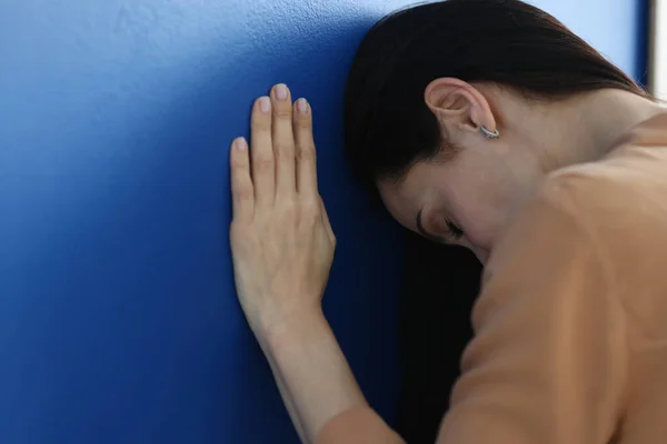 Mujer triste de pie con la cabeza inclinada cerca de la pared azul —  Fotos de Stock