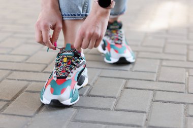 Kadın eli bağcıkları çok renkli spor ayakkabılara bağlıyor.