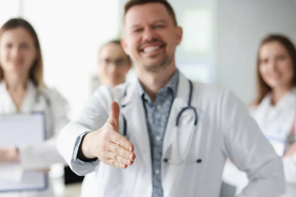 Hombre médico mostrando pulgar hacia arriba contra los antecedentes de colegas en la clínica —  Fotos de Stock