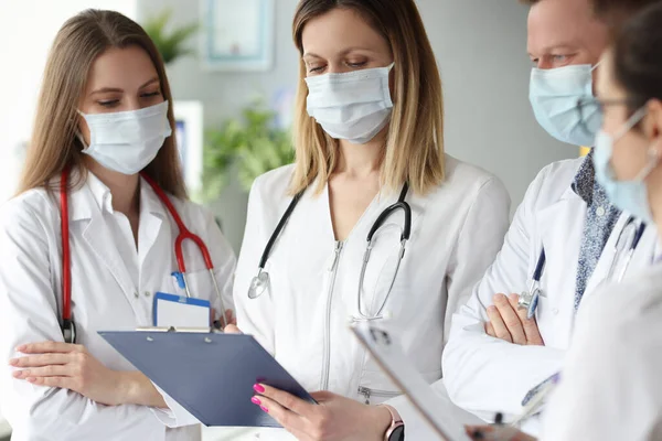 Groep artsen in medische beschermende maskers staan met klemborden met documenten in de kliniek — Stockfoto