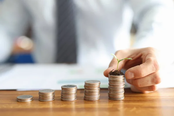 Before businessman stands pyramid of coins in ascending order on last pyramid