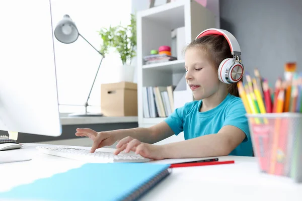 Kleines Mädchen mit Kopfhörern vor dem Computer tippt auf Tastatur — Stockfoto