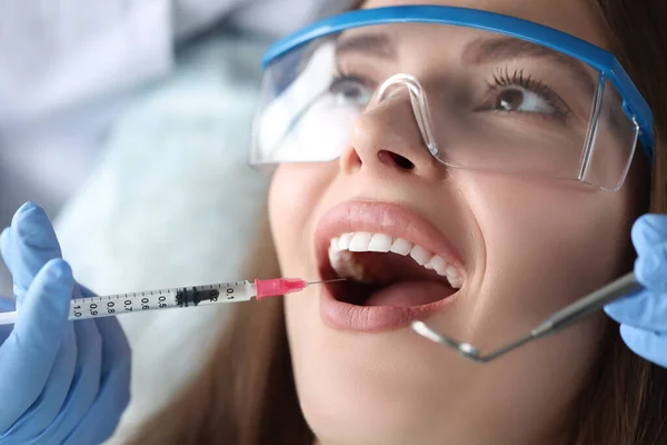 Dentist making injection in gum of female patient in clinic
