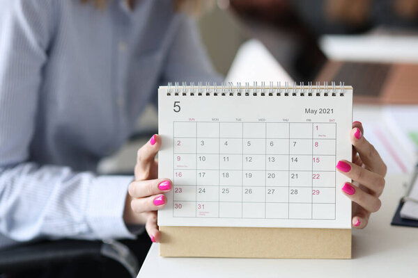 Female hands with pink manicure holding looseleaf paper calendar closeup
