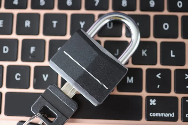 Padlock with key lying on laptop keyboard closeup