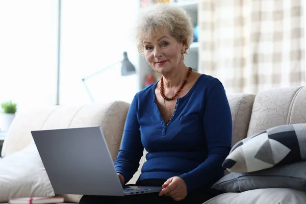 Elderly woman with laptop is sitting on couch