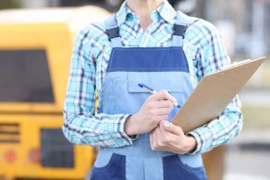 Tulumlu kadın müteahhit elinde pano ve tükenmez kalemle yakın çekim yapıyor.