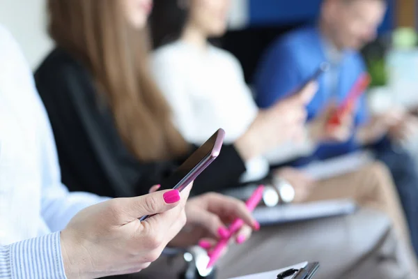 Žena sedí na židli a drží telefon v rukou na pozadí kolegů detailní up — Stock fotografie