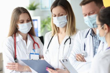 Koruyucu tıbbi maskeli bir grup doktor ellerinde belgelerle klinikte duruyorlar.