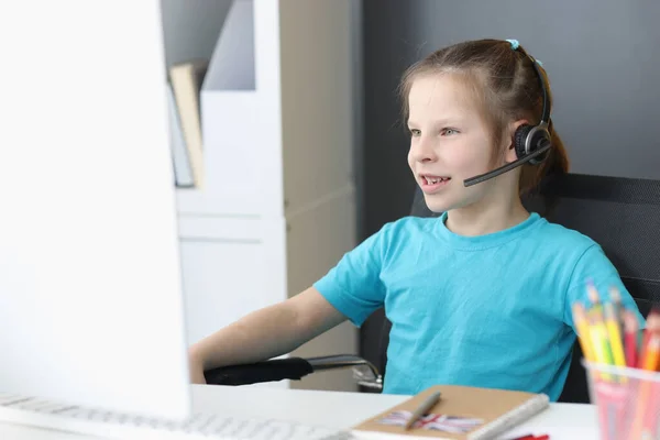 Niña en auriculares con micrófono sentado frente a la pantalla del ordenador —  Fotos de Stock