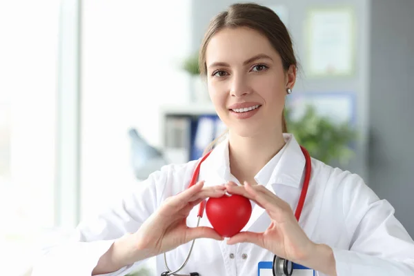 微笑的女医生，手里拿着红心玩具在诊所里 — 图库照片