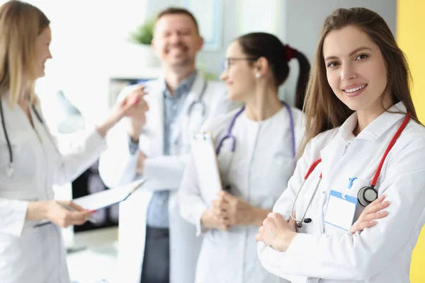 Mujer sonriente médico con estetoscopio rojo de pie sobre el fondo de los colegas —  Fotos de Stock