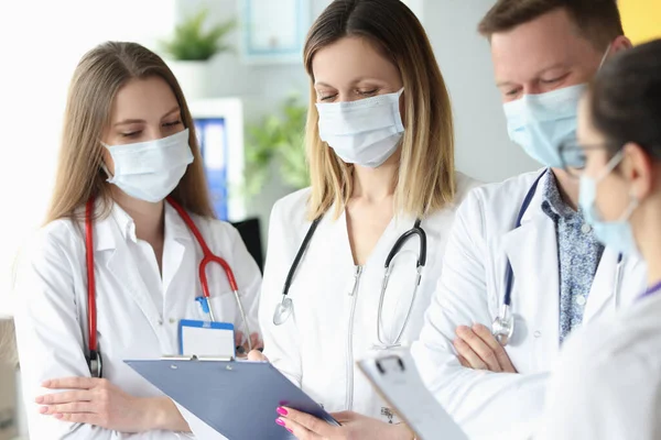 Groep artsen in beschermende medische maskers staan met documenten in hun handen in de kliniek — Stockfoto