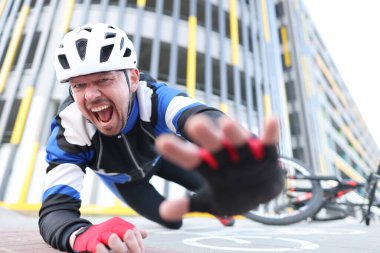 Kasklı bisikletçi bisikletten düşüp bağırıyor.