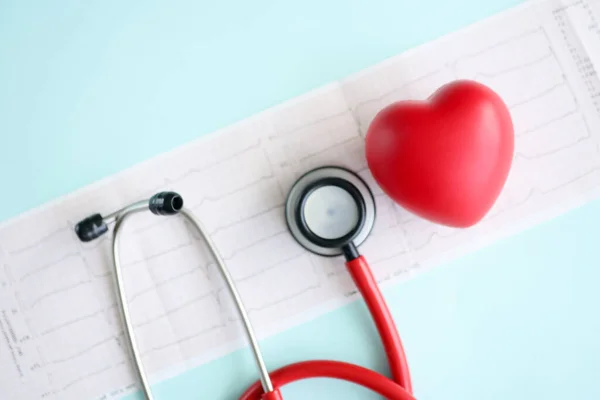Красное игрушечное сердце и стетоскоп лежат на кардиограмме крупным планом — стоковое фото