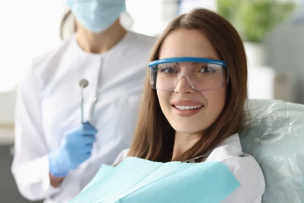 Женщина в защитных очках сидит в стоматологическом кресле рядом с доктором — стоковое фото