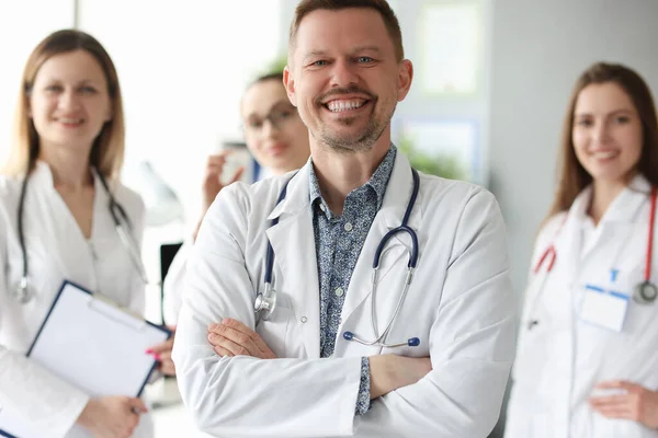 Framgångsrik leende man läkare står mot bakgrund av kollegor på kliniken — Stockfoto