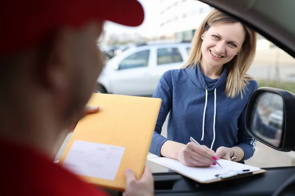 Vrouwelijke klant zet handtekening op documenten bij ontvangst pakket van koerier — Stockfoto