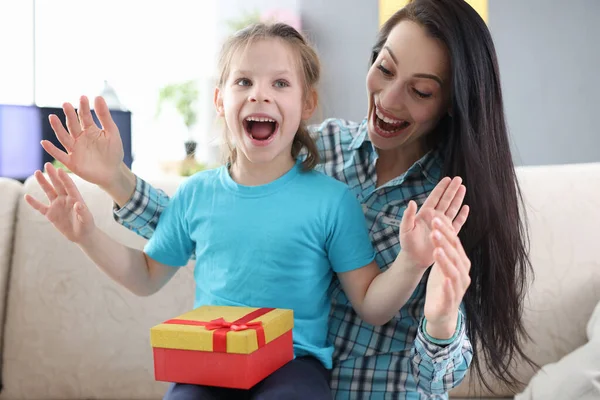 Entusiastiska mamma och dotter med presentförpackning sitter på soffan — Stockfoto