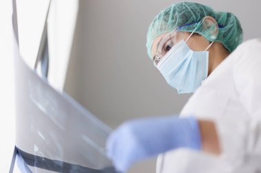 Koruyucu maske ve eldiven takan doktor röntgen görüntülerini inceliyor.