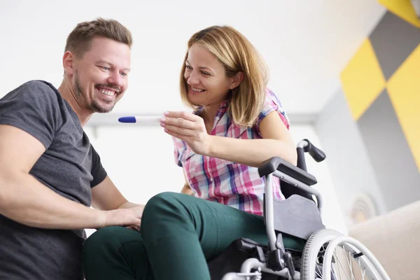 Щаслива жінка в інвалідному візку, що показує тест на вагітність чоловікові — стокове фото