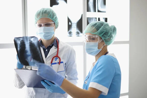 Dwóch lekarzy w ochronnych maskach medycznych bada prześwietlenie pacjenta. — Zdjęcie stockowe