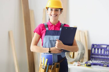 Gülümseyen kadın müteahhit elinde belgelerle pano tutuyor.