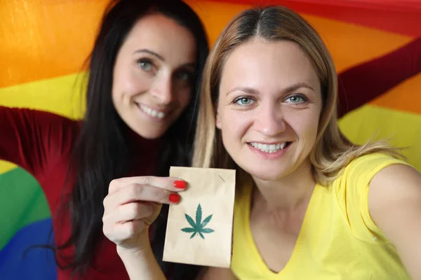 Dos mujeres sonrientes sosteniendo bandera lgbt y paquete de marihuana — Foto de Stock