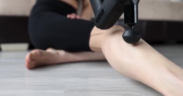 Femme assise sur le sol et massant sa jambe avec un masseur à percussion film 4k — Video