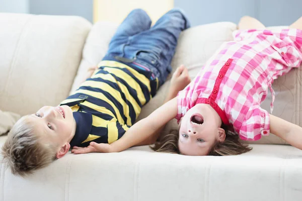 Menino e menina deitados no sofá de cabeça para baixo em casa — Fotografia de Stock