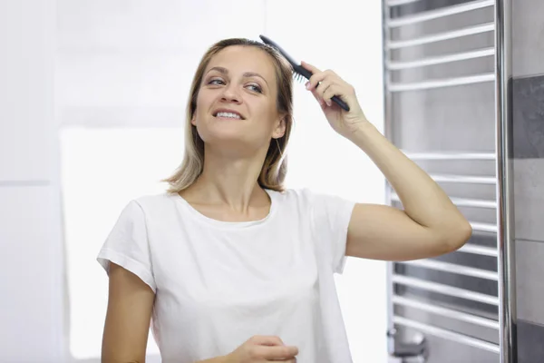 Giovane donna sorridente pettinarsi i capelli in bagno — Foto Stock