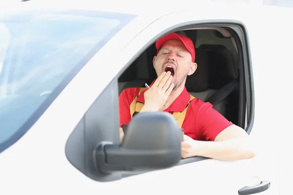 Muž kurýr sedí za volantem auta a zívá — Stock fotografie
