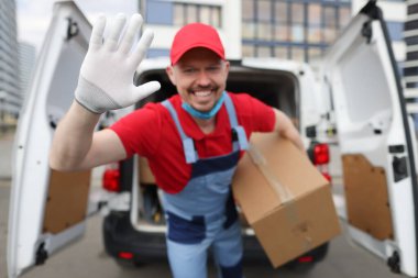 Erkek kurye karton kutu tutuyor ve yakın çekim için el sallıyor.