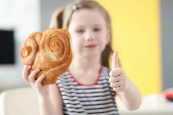 Menina comendo pão grande e mostrando o polegar de perto — Fotografia de Stock