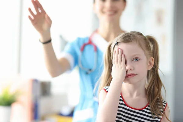 Mała dziewczynka zakrywa oczy dłonią podczas wizyty u okulisty. — Zdjęcie stockowe
