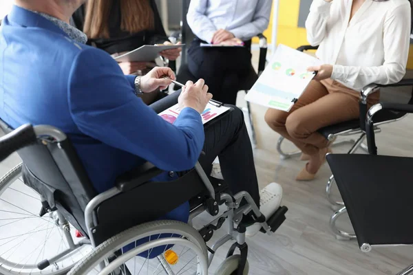 Behinderter Mann mit Dokumenten in der Hand sitzt im Rollstuhl vor dem Hintergrund von Kollegen Nahaufnahme — Stockfoto