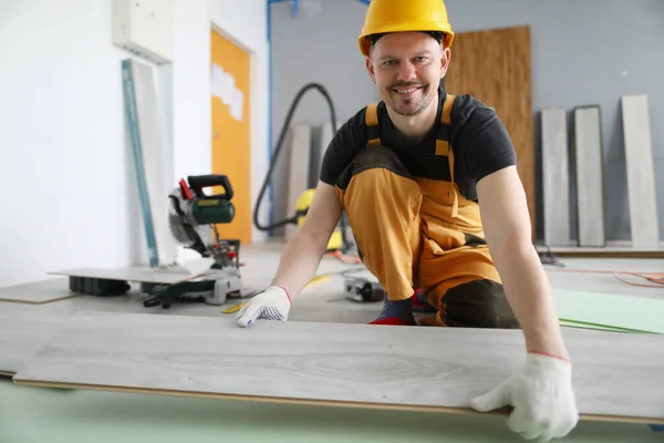 Smiling male construction worker is laying new floor covering — Stock Photo, Image