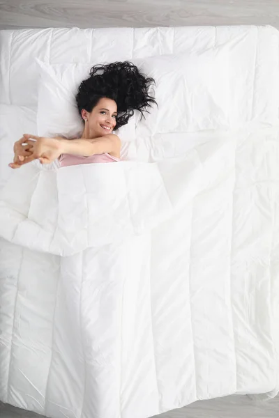 Vacker ung leende kvinna ligger på stor säng med vit pastell linne — Stockfoto
