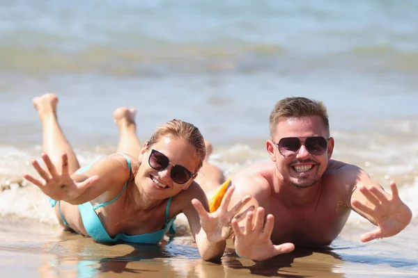 Gioioso uomo e donna in occhiali da sole si trovano sulla sabbia bagnata vicino al mare — Foto Stock