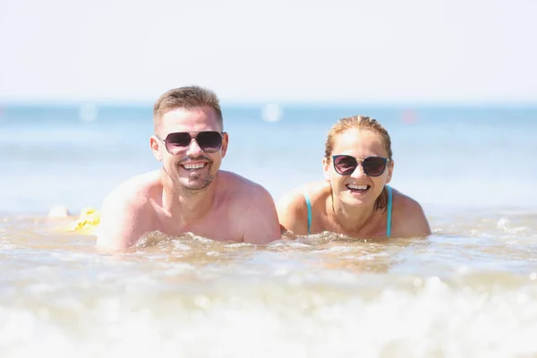 Felice uomo e donna sorridente in occhiali da sole si trovano sulla riva del mare — Foto Stock