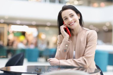 Kahvede otururken akıllı telefondan konuşan gülümseyen kadın.