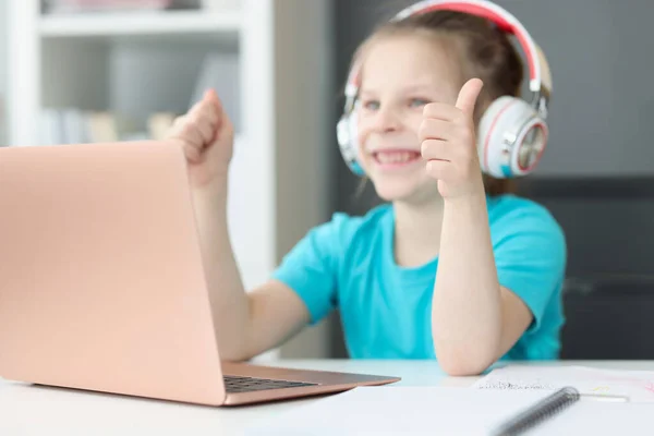 Sorrindo menina senta-se no laptop em fones de ouvido e mostra polegares para cima — Fotografia de Stock