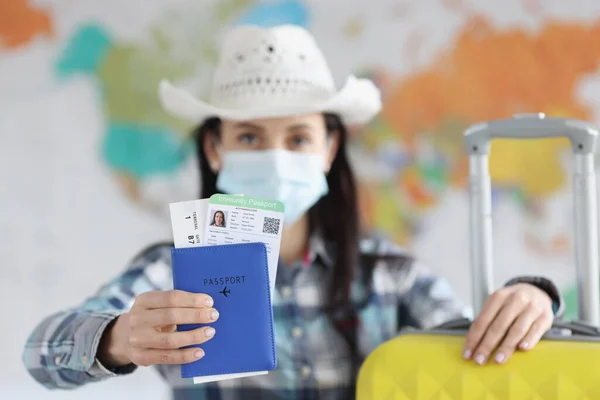 Woman in medical protective mask and suitcase shows her passport holds passport immunity from coronavirus infection — Stock Photo, Image