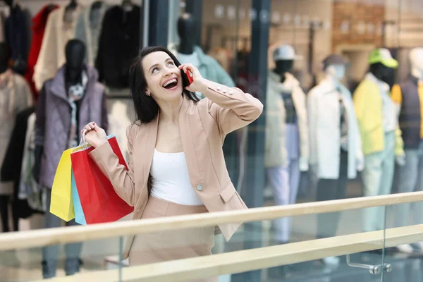 Vidám nő beszél okostelefonon, és tartsa bevásárló táskák a plázában — Stock Fotó